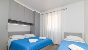 Ett hotellrum med två sängar, var och en med ett blått överkast och vita kuddar. Det finns en inbyggd garderob med en spegel och en hylla med dekorativa föremål.