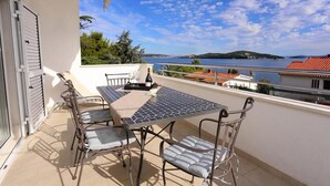 Un balcon avec une table et des chaises, donnant sur une étendue d’eau et une côte lointaine.