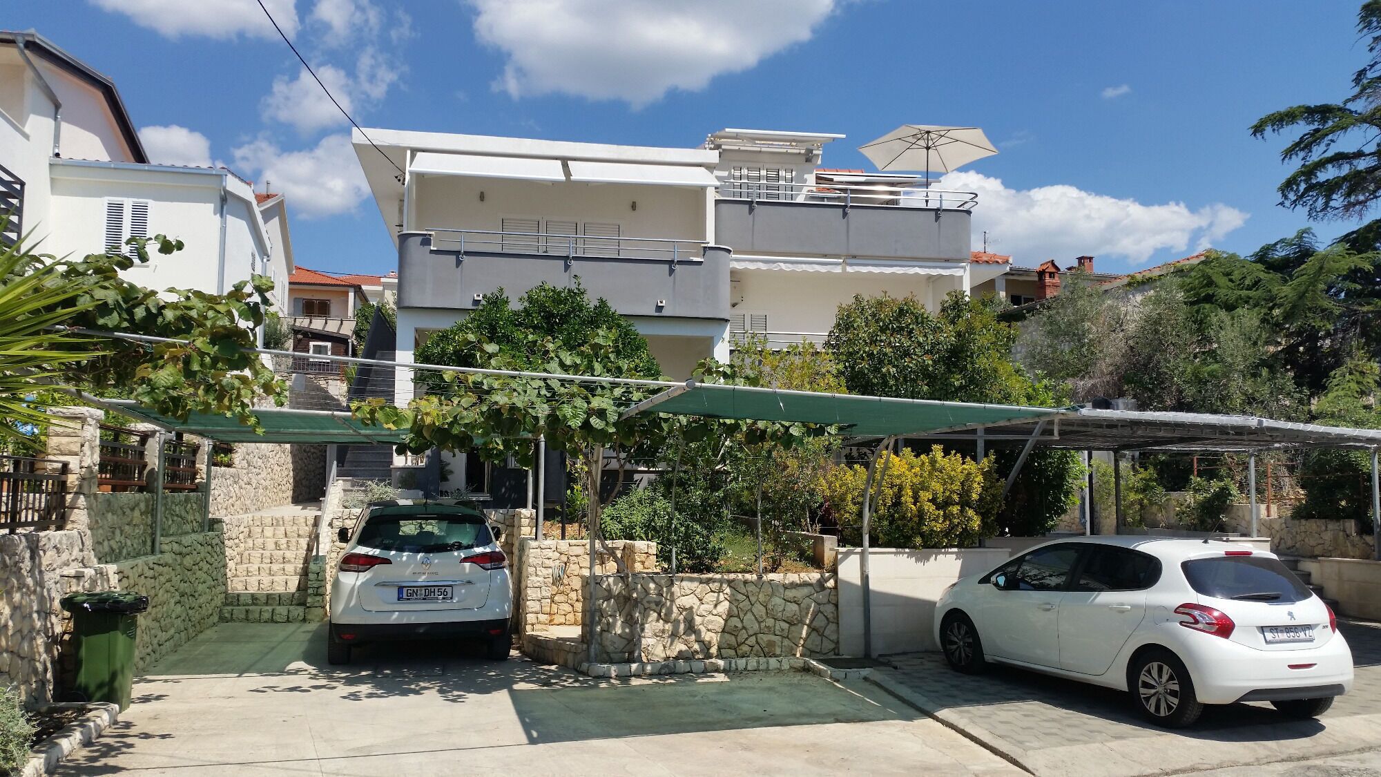 Un quartier résidentiel avec deux voitures garées, un mur en pierre et un immeuble doté d’un balcon.