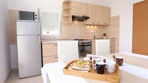Une cuisine compacte équipée d’un réfrigérateur, d’une cuisinière, d’un four et de meubles de rangement en bois. Un plateau de petit-déjeuner avec du pain, des tasses à café et une théière est posé sur la table.