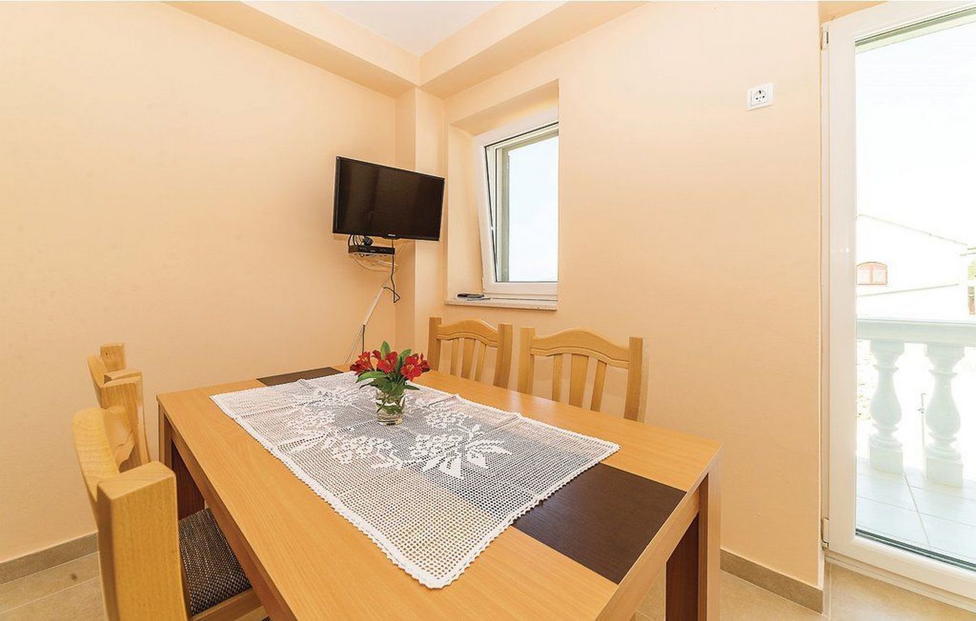 Un comedor con una mesa de madera, mantel de encaje blanco y un florero con flores.