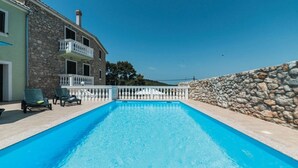 Una piscina con un muro de piedra en un lado y un edificio con balcón en el otro.