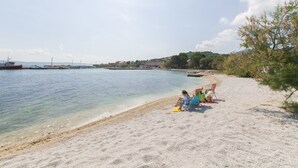 Una playa con agua cristalina, orilla arenosa y algunos barcos a lo lejos.