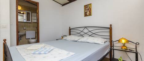 A bedroom with a bed, a nightstand with a lamp, a wooden headboard, a mirror, and a picture on the wall.