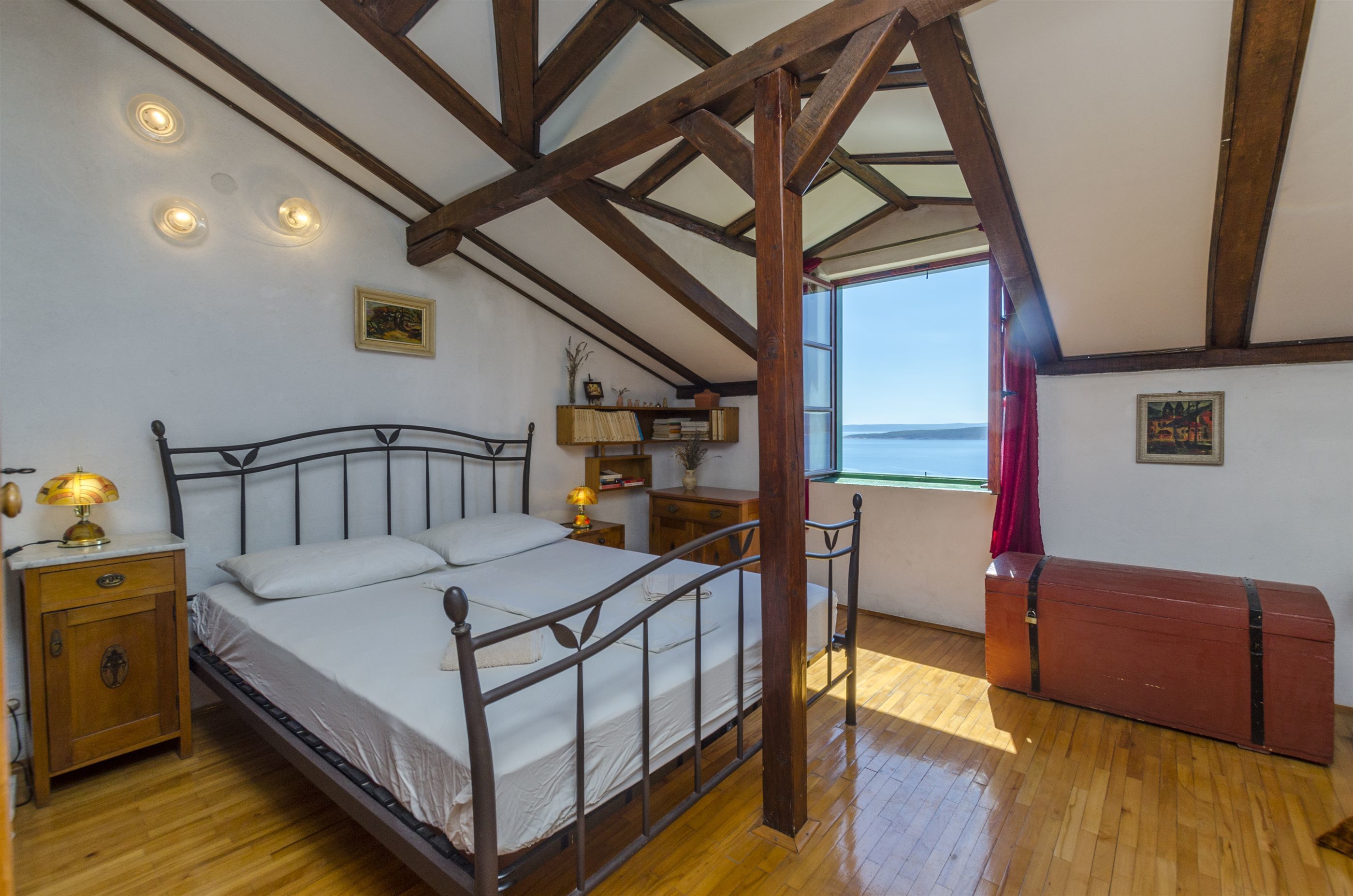 A bedroom with a wooden ceiling, a bed, bedside tables, a nightstand, a dresser, and a window with a view.