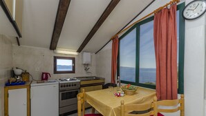 A compact kitchen with a dining area, a window with curtains, and a wall clock. - Apartment Boris (Brela)