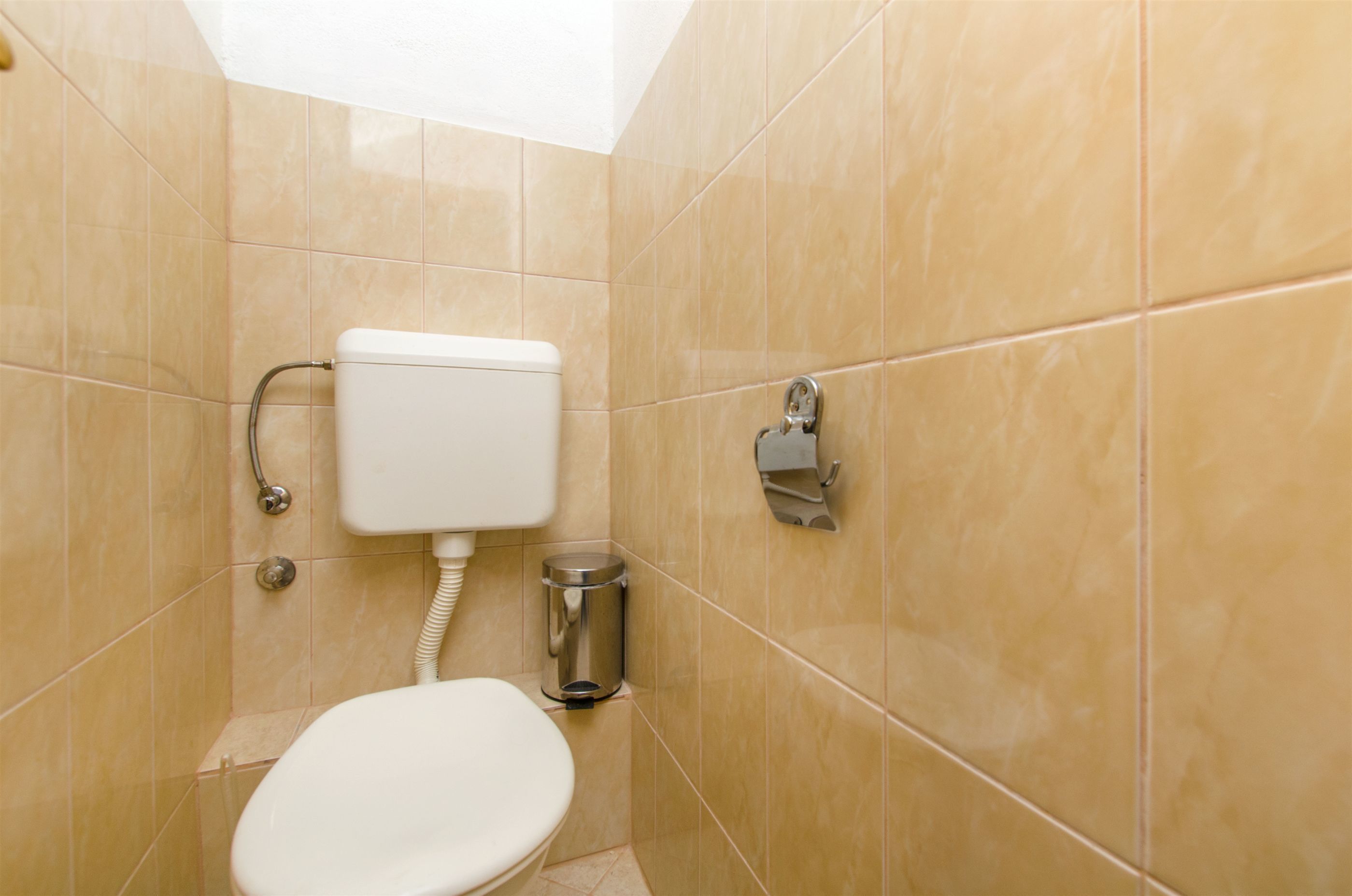 A small, tiled bathroom with a toilet, a trash can, and a paper towel dispenser.