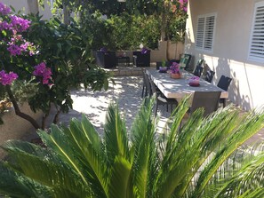 En patio med borde og stole, omgivet af krukker med planter og blomstrende træer.