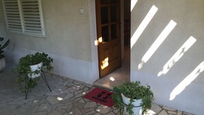 Uma entrada de casa com varanda de pedra, porta de madeira e dois vasos de plantas.