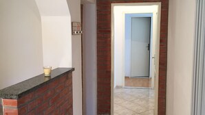 Um corredor com parede de tijolos decorativa, piso de azulejos e uma porta que dá para outro cômodo.