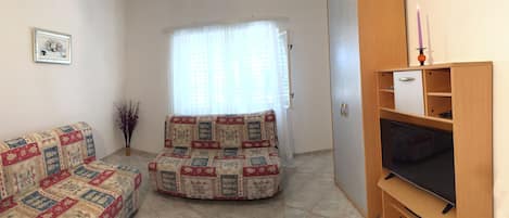 A living room with a sofa, a chair, a TV, and a window with curtains.