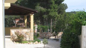 A covered outdoor area with a stone wall, a small tree, and a gravel path. - Apartment Deni (Milna)