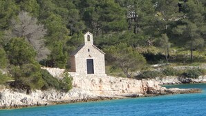 A stone chapel with a bell tower, surrounded by dense trees and a rocky shoreline. - Apartment Deni (Milna)