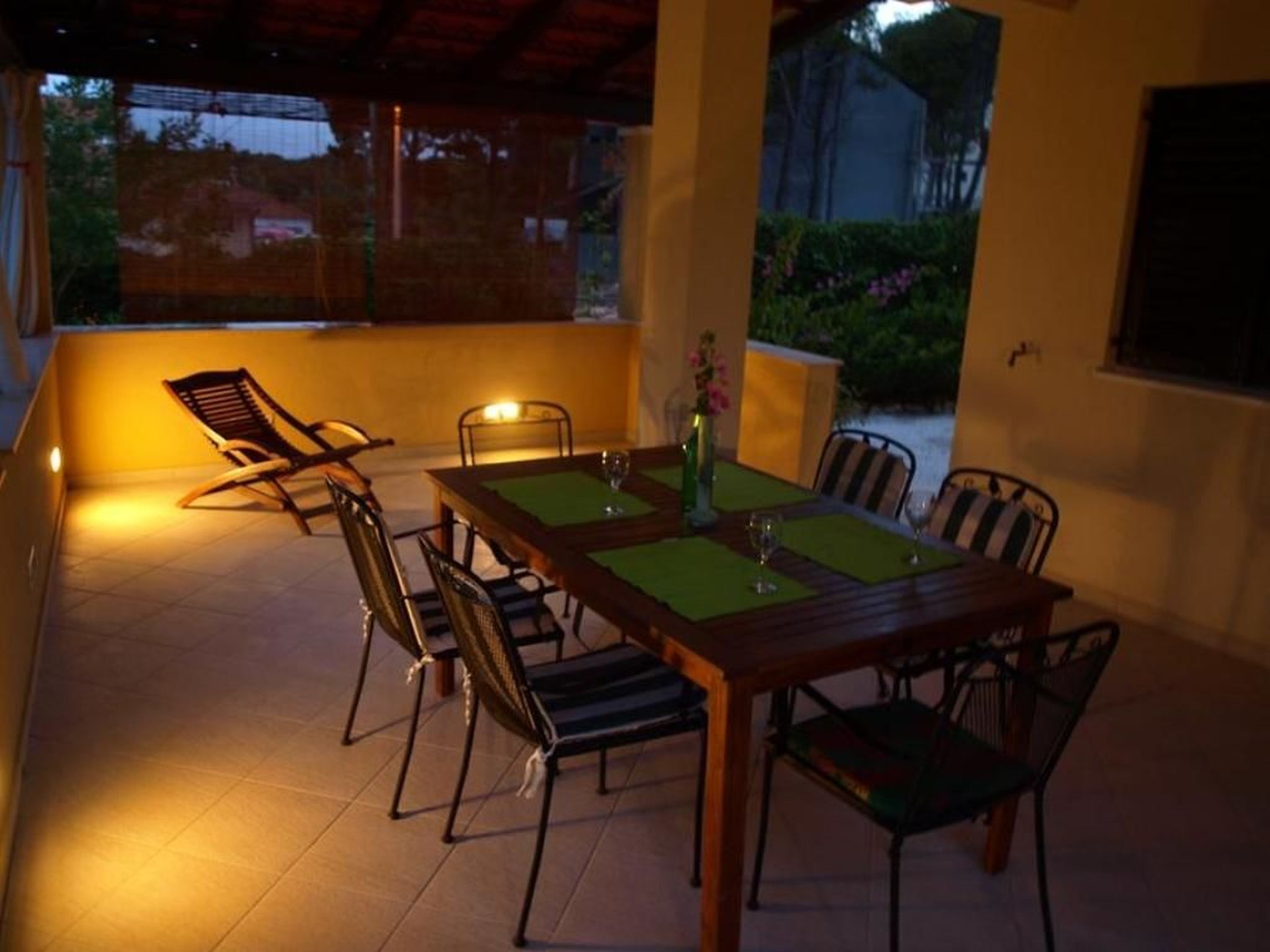 An outdoor dining area with a wooden table and chairs, a vase with flowers, and a view of the surrounding landscape.