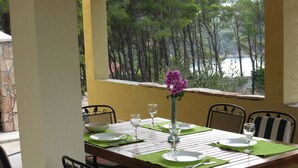 A dining table set for four with green placemats, white plates, and clear wine glasses. - Apartment Deni (Milna)