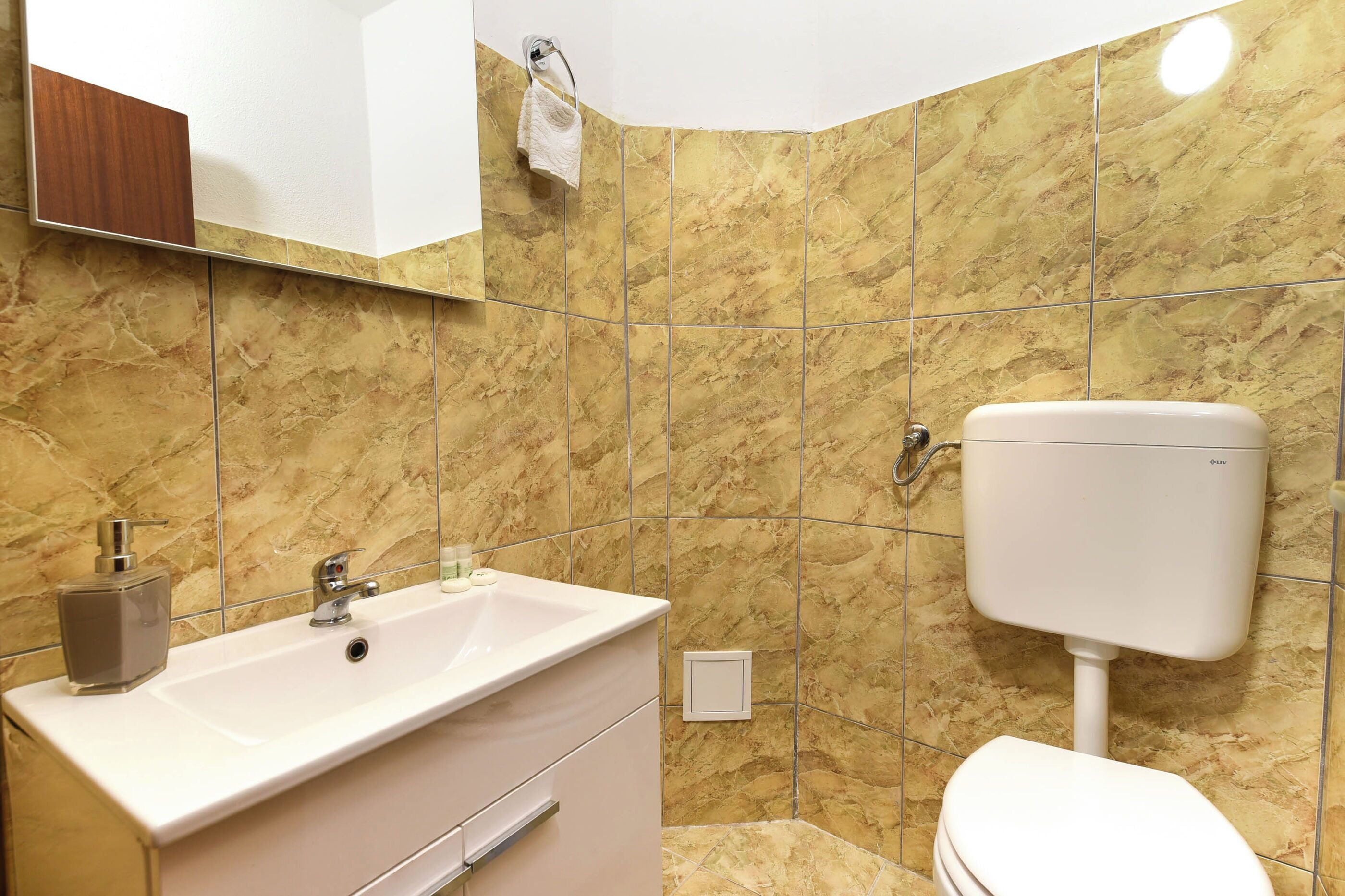 Un baño con lavamanos blanco, inodoro y paredes de mármol.
