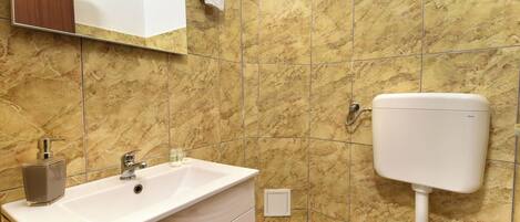 Un baño con lavamanos blanco, inodoro y paredes de mármol.