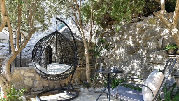 A stone wall, a hanging chair, a metal table, and a metal chair in an outdoor setting. - House Villa Danica (Podstrana)