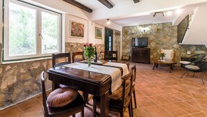 A dining area with a stone wall, wooden furniture, and a television in the background. - House Villa Danica (Podstrana)