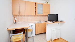 A compact kitchen with wooden cabinets, a built-in microwave, a sink, and a small dining area with a chair. - Apartment Marijo (Split)