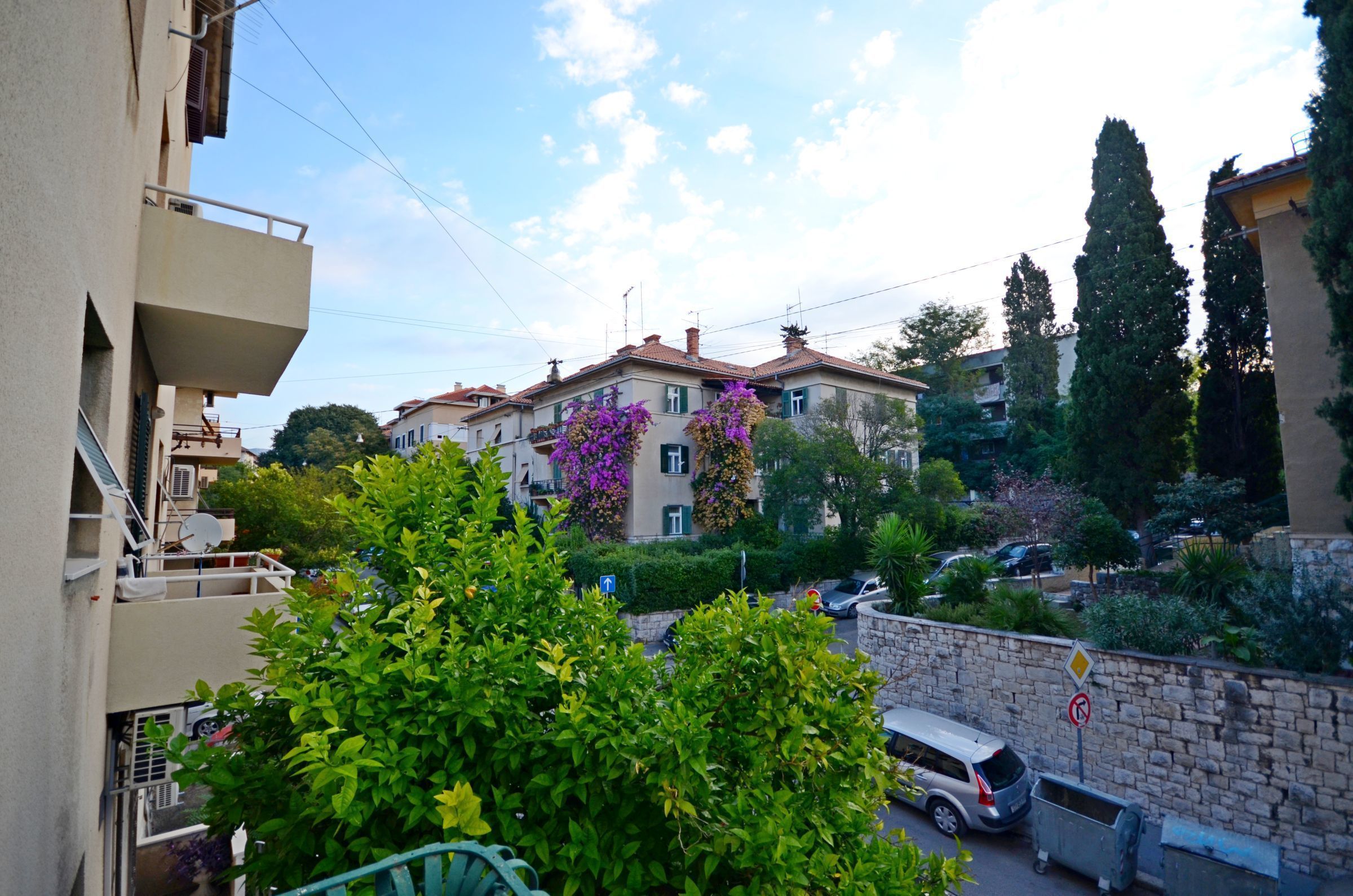 Un edificio residencial con balcones, una pared de piedra y automóviles estacionados.