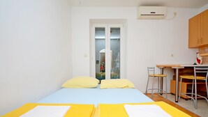 A room with two beds, a small kitchenette, and a window with a view of a building. - Apartment Marijo (Split)