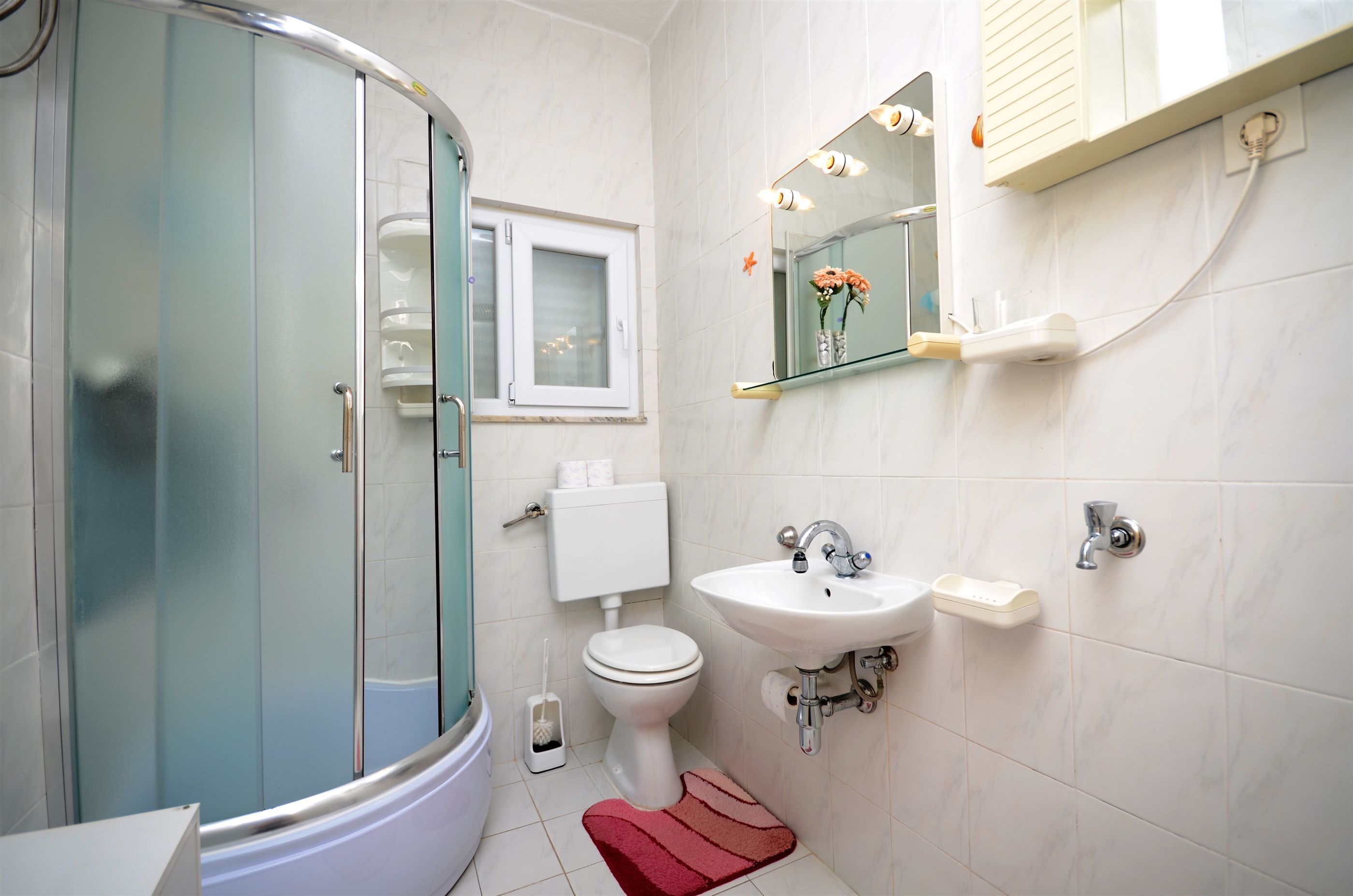 A bathroom with a glass-enclosed shower, a toilet, a sink, and a mirror with lights.