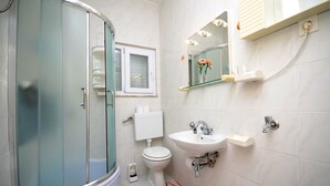 A bathroom with a glass-enclosed shower, a toilet, a sink, and a mirror with lights. - Apartments Marijo (Sevid)