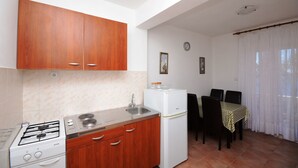 A compact kitchen with wooden cabinets, a white refrigerator, and a gas stove. - Apartments Marijo (Sevid)