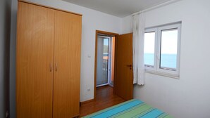 A bedroom with a large wardrobe, a bed with a striped bedspread, a window with a view of the sea, and a door leading to another room. - Apartments Marijo (Sevid)