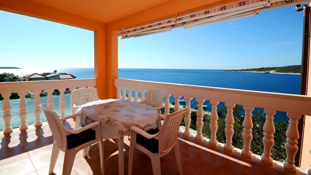 A balcony with a table and chairs, overlooking a clear blue sea and a distant coastline. - Apartments Marijo (Sevid)