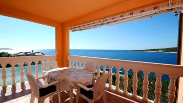 A balcony with a table and chairs, overlooking a clear blue sea and a distant coastline.