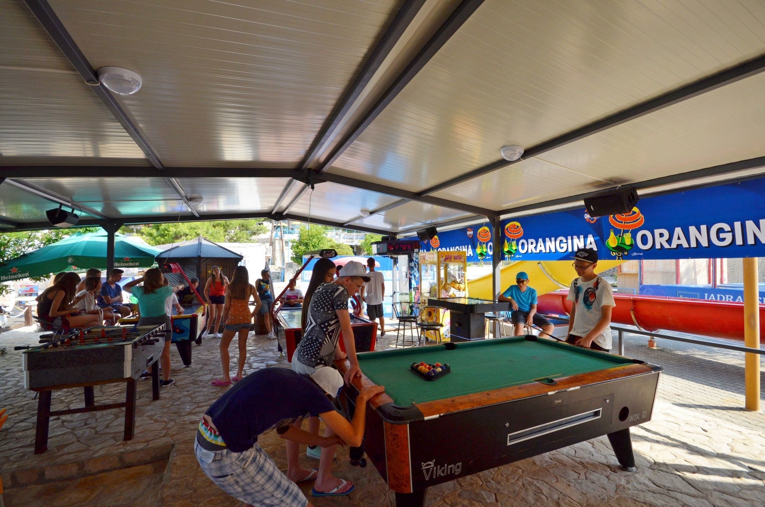 Un espace extérieur aménagé avec une table de billard, protégé par un toit, et où l’on peut voir des gens jouer au billard.