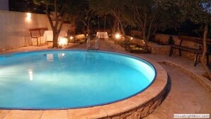Une piscine ronde, bordée de pierres, entourée d’arbres et dotée d’un espace salon extérieur.