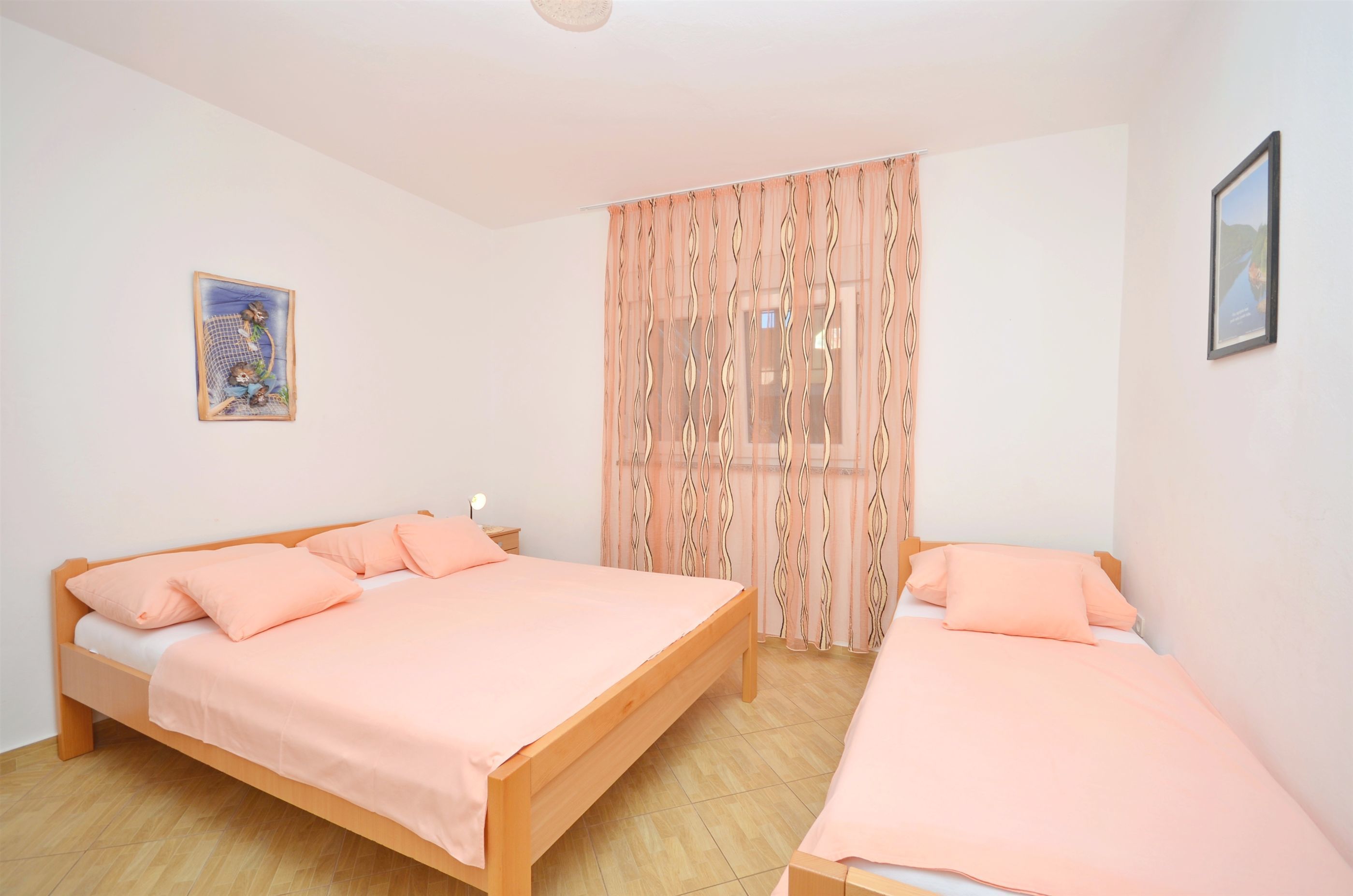 Une chambre à coucher avec deux lits en bois, chacun agrémenté d’une literie de couleur pêche, une table de chevet et un tableau accroché au mur.