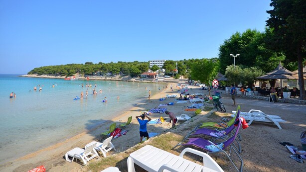 Une plage avec des transats, quelques personnes qui se baignent et un bâtiment en arrière-plan.