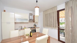 Une cuisine moderne avec des meubles blancs, une table à manger en bois et une vue sur un balcon agrémenté de rideaux.