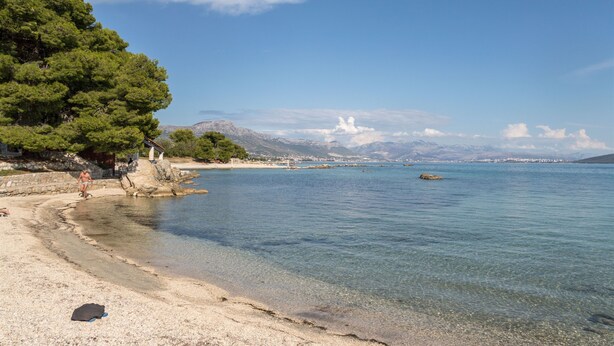 Egy tiszta vizű strand, sziklás parttal, és a háttérben egy hegy.