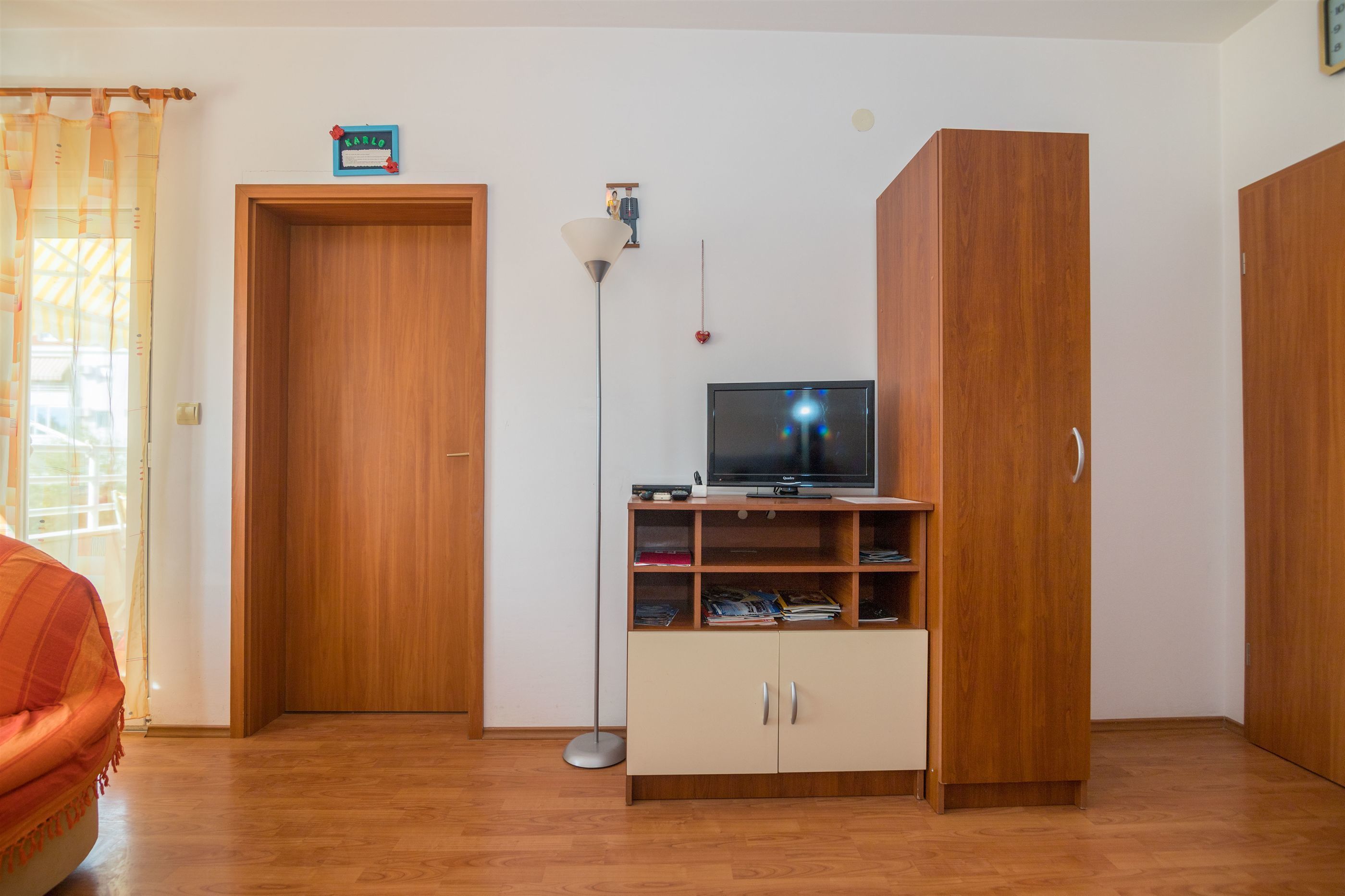A room with a wooden floor, a TV on a wooden stand, a wardrobe, and a door.