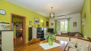 A dining area with a wooden table, chairs, and a vase of flowers. There is a sofa with floral cushions in the background. - Apartments Ante (Igrane)
