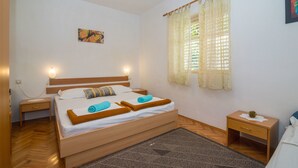 A neatly arranged bedroom with a wooden bed, a nightstand, a bedside table, and a window with curtains. - Apartments Ante (Igrane)