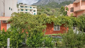 A building with a red facade, surrounded by greenery and a mountainous backdrop. - Apartments Ante (Igrane)