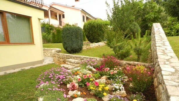 Un jardín con diversas flores y un muro de piedra.