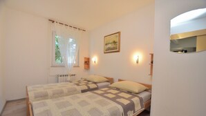 Un dormitorio con dos camas, una ventana con cortinas translúcidas, un cuadro en la pared y lámparas de noche.