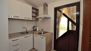 Una cocina con armarios blancos, un lavamanos de acero inoxidable, una estufa empotrada y una puerta con marco negro.
