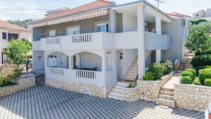 Une maison à deux étages avec un balcon, des marches en pierre et une allée carrossable dallée.