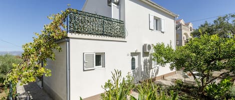 A two-story house with a balcony, potted plants, and a clear sky.
