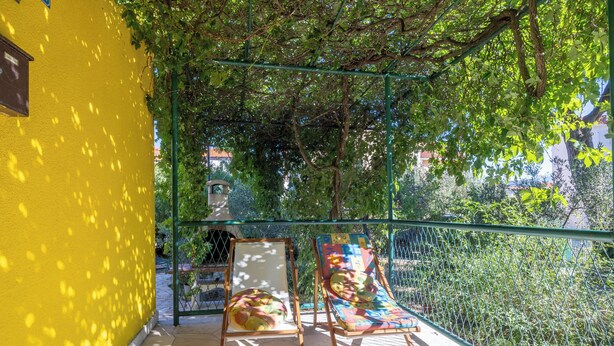 Un balcone con due sdraio e un tavolino, circondato da una recinzione verde e alberi.