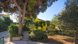 Una casa gialla con un vialetto in pietra che conduce all'ingresso, circondata da vegetazione e alberi.