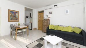 Un soggiorno con un divano nero, un tavolo da pranzo in legno con sedie, un piccolo tavolino bianco e un quadro appeso al muro.
